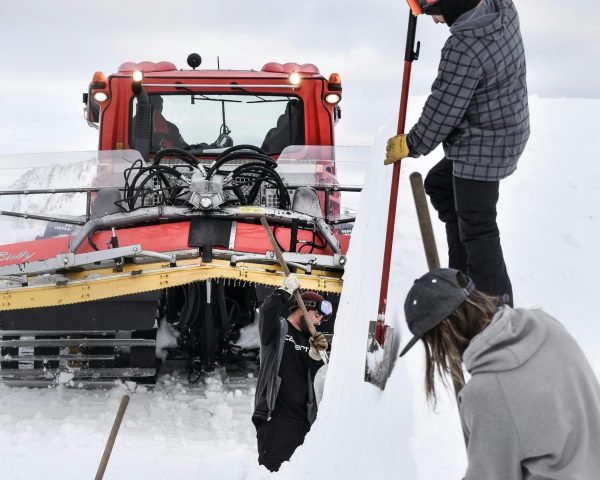 People clearing snow with shovels and a snowcat on a winter day.